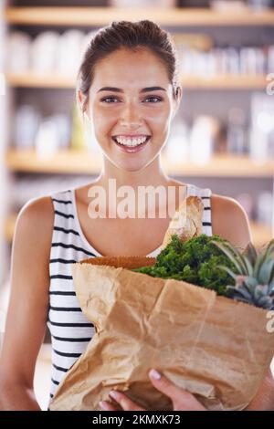 Ich fange mit meiner neuen Diät an. Eine attraktive Frau, die eine Tüte Lebensmittel in der Küche hält. Stockfoto