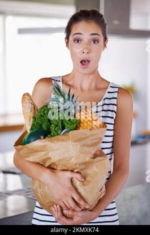 Gesundes Essen macht mich aufgeregt. Eine attraktive Frau, die eine Tüte Lebensmittel in der Küche hält. Stockfoto