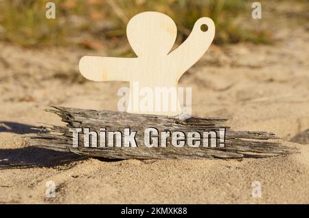 Ökologie. Auf dem Sand in der Nähe der hölzernen Figur eines Mannes befindet sich ein Stück Holz mit der Inschrift "Think Green" Stockfoto