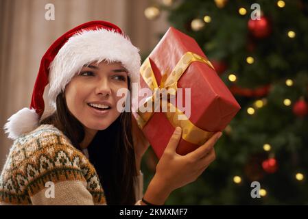 Was könnte das sein? Eine attraktive junge Frau, die versucht, das Geschenk herauszufinden, das sie am Weihnachtsmorgen bekam. Stockfoto