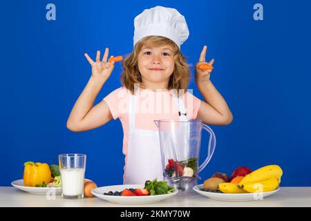 Kinderkoch isoliert auf blau. Lustige kleine Köchin Koch trägt Uniform Kochmütze und Schürze und hält Karotten gekochtes Essen in der Küche. Stockfoto