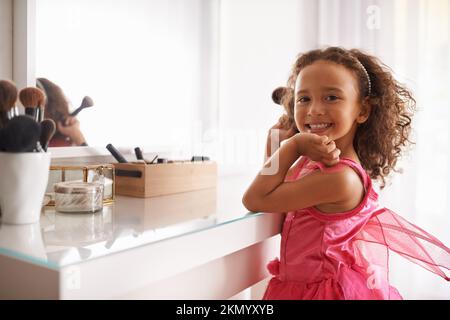 Ich werde genauso aussehen wie meine Mami. Porträt eines kleinen Mädchens, das einen Blusher im Spiegel aufträgt. Stockfoto