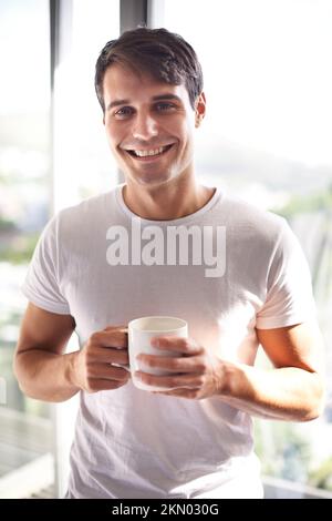 Es geht nichts über eine frische Tasse Kaffee am Morgen. Porträt eines gutaussehenden jungen Mannes, der Kaffee trinkt, während er an seinem Schlafzimmerfenster steht. Stockfoto