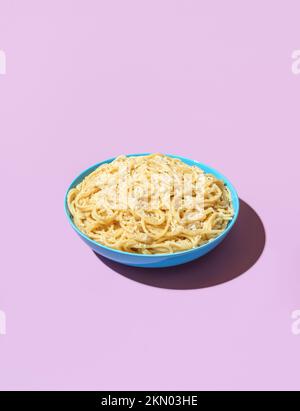 klassisches italienisches Gericht, Spaghetti mit geriebenem Parmesan und schwarzem Pfeffer, minimalistisch auf einem violetten Tisch. Pasta Cacio e Pepe in einer blauen Schüssel auf einem bunten B Stockfoto