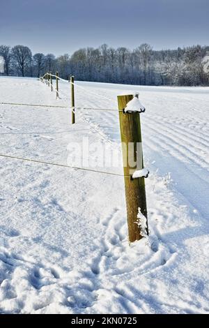 Frostiger Zaun. Ein Zaun am Straßenrand einer schneebedeckten Landschaft. Stockfoto