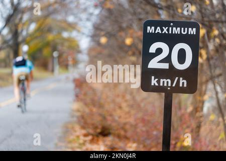 Geschwindigkeitsbegrenzungsschild, 20 km/h für Fahrradwege im Park. Radweg mit Radfahrer im Herbst. Stockfoto