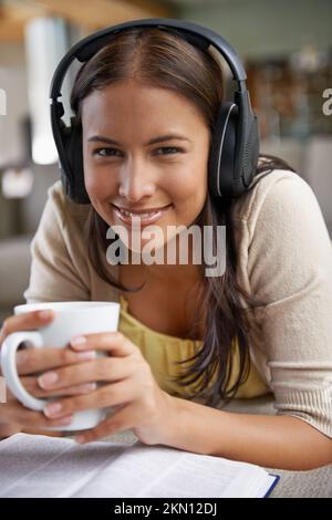 Musik und Kaffee sind die besten Freundinnen. Eine attraktive junge Frau, die Musik über ihre Kopfhörer hört, während sie Kaffee trinkt und liest. Stockfoto