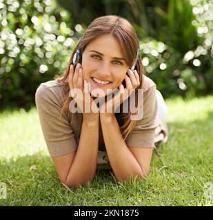 Ich genieße die Symphonie der Natur. Eine wunderschöne junge Frau, die auf dem Rasen liegt und Musik hört. Stockfoto