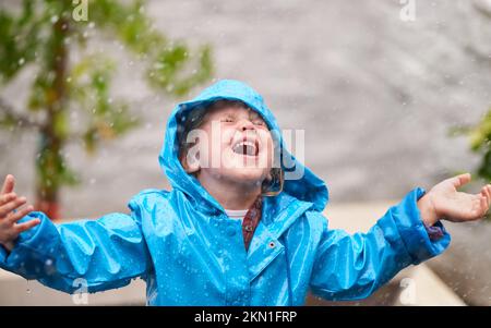 Ich singe im Regen... ein bezauberndes kleines Mädchen, das draußen im Regen spielt. Stockfoto