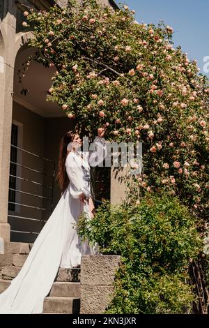 Eine schöne Frau in einem weiß fließenden langen Kleid bleiben in der Nähe eines schönen Feldes mit rosa Blumen Rückansicht Stockfoto