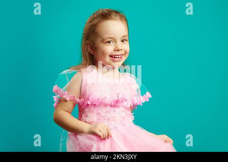 Lächelndes Mädchen in rosa Kleid auf blau isoliert Stockfoto