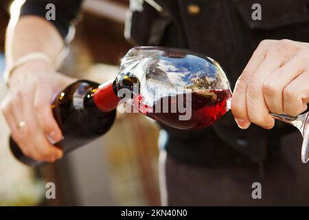 Mann gießt Wein in Weinglas, männliche Hand hält Flasche Stockfoto