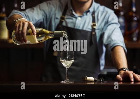 Sommeliermännchen gießt Weißwein in langstielige Weingläser. Stockfoto