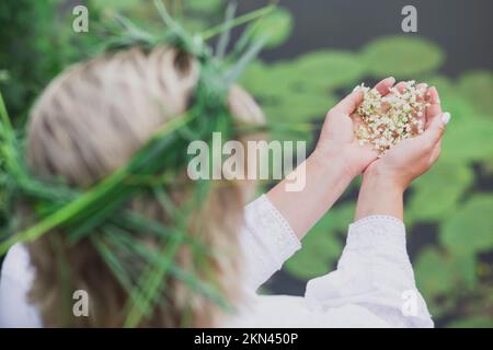 Eine Frau im Nachthemd mit Kranz hält Holunderblüten in der Hand Stockfoto