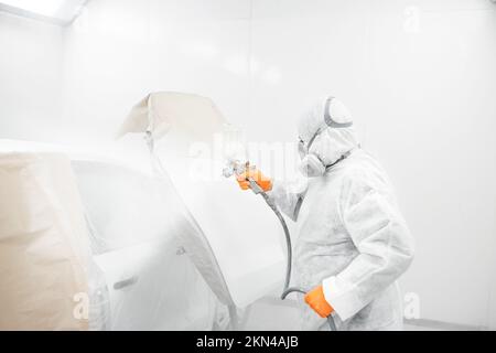 Professioneller, männlicher Autolacker malt in der Garage mit einer Airbrush. Arbeiter lackiert Fahrzeug mit Sprühpistole. Stockfoto