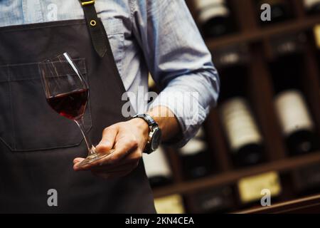 Männlicher Sommelier hält Bokal mit Rotwein in der Hand Stockfoto