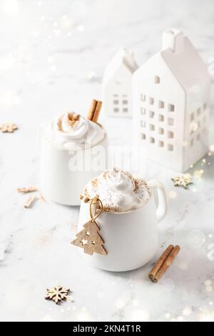Zwei Tassen heiße Schokolade oder Kakao mit Schlagsahne und Zimt auf weißem Marmorhintergrund mit Bokeh-Lichtern. Festliches Weihnachtsmodell, Karte Stockfoto