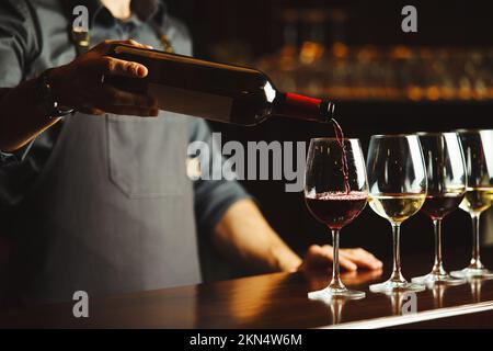 Der Barkeeper gießt Rotwein in Gläser auf einer Holztheke ein Stockfoto