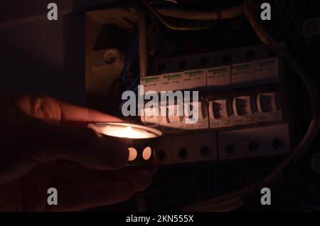 Blackout-Konzept. Die Hand einer Person in völliger Dunkelheit hält eine Taschenlampe in der Hand, um einen Sicherungskasten im Haus während eines Stromausfalls zu untersuchen. Stockfoto