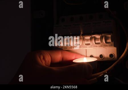 Blackout-Konzept. Die Hand einer Person in völliger Dunkelheit hält eine Taschenlampe in der Hand, um einen Sicherungskasten im Haus während eines Stromausfalls zu untersuchen. Stockfoto