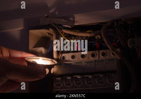 Blackout-Konzept. Die Hand einer Person in völliger Dunkelheit hält eine Taschenlampe in der Hand, um einen Sicherungskasten im Haus während eines Stromausfalls zu untersuchen. Stockfoto