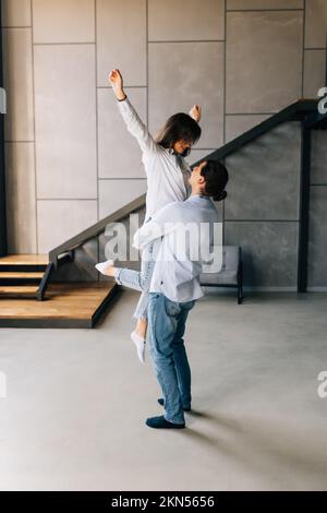 Glückliches, liebevolles Paar, das sich küsst, sich aufgeregt fühlt, in ein neues Zuhause zu ziehen, ein Mann, der eine Frau in den Händen hält, indem er beginnt, zusammen zu leben Stockfoto