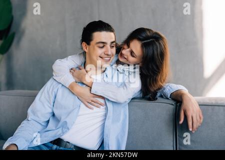 Porträt eines Paares, das umarmt und in die Kamera schaut, sitzt auf dem Sofa. Stockfoto