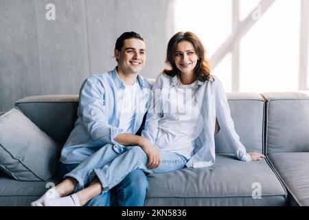 Liebevolles Paar, das auf der Couch im Wohnzimmer sitzt, kuschelt und zärtliche süße Momente zusammen genießt, während des romantischen Wochenendes auf dem Sofa entspannen Stockfoto