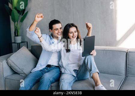 Aufgeregtes Paar, das Tablet und Quittungen überprüft, sitzt auf dem Sofa im Wohnzimmer zu Hause Stockfoto