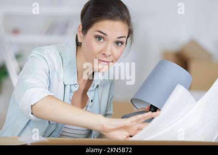 Frau, die die Lampe aus dem Umzugskasten in einem neuen Haus entfernt Stockfoto