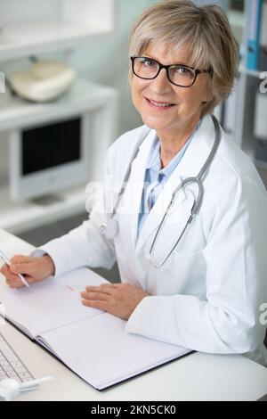 Leitende Ärztin trägt eine Brille, um Papierkram zu erledigen Stockfoto