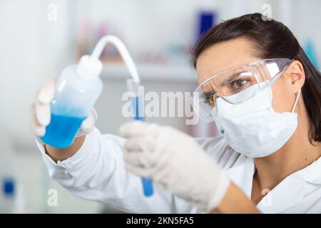 Leitende Chemikerin in Schutzbrillen mischt Flüssigkeiten Stockfoto