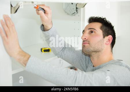 Handwerker, der eine Tür am Schrank repariert Stockfoto