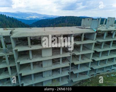 Das mehrstöckige verlassene Hotel mit Betonwänden befindet sich in einem dichten Fichtenwald am Hang des hohen Tals der Rhodope Mountains Stockfoto