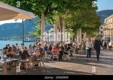 Gardasee Italien, Blick auf die Menschen, die sich an Cafétischen entlang der Uferpromenade in der malerischen Altstadt von Gardasee, Gardasee, Veneto entspannen Stockfoto