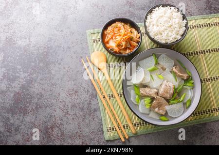 muguk leichte, nahrhafte südkoreanische Suppe kombiniert Stücke von Rindfleisch und geschnittenen koreanischen Radieschen Mu serviert mit Reis und Kimchi-Nahaufnahme auf der Matte des Stockfoto