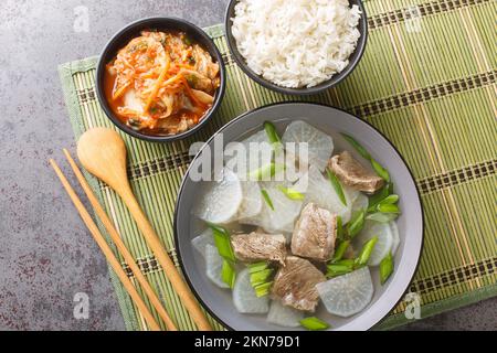 Koreanische Rindfleisch-Rettich-Suppe, soegogi muguk genannt, serviert mit Reis und Kimchi Nahaufnahme auf der Matte auf dem Tisch. Horizontale Draufsicht von oben Stockfoto