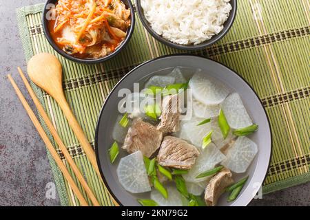 Seogogi Mu Guk Koreanisches Rindfleisch und Rettich-Suppe serviert mit Reis und Kimchi Nahaufnahme auf der Matte auf dem Tisch. Horizontale Draufsicht von oben Stockfoto