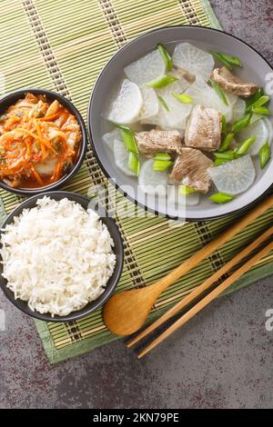 Koreanische Rindersuppe Sogogi Muguk serviert mit Reis und Kimchi Nahaufnahme auf der Matte auf dem Tisch. Vertikale Draufsicht von oben Stockfoto