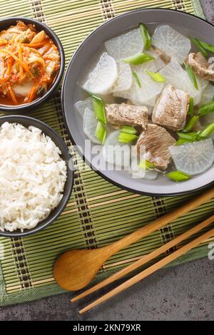 Soegogi muguk Beef and Radieschen Suppe ist eine sehr beliebte Suppe in Korea, serviert mit Reis und Kimchi Nahaufnahme auf der Matte auf dem Tisch. Vertikale Draufsicht von Stockfoto