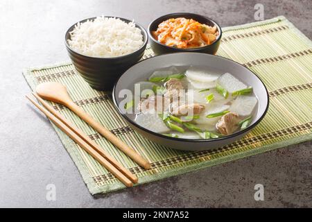 muguk leichte, nahrhafte südkoreanische Suppe kombiniert Stücke von Rindfleisch und geschnittenen koreanischen Radieschen Mu serviert mit Reis und Kimchi-Nahaufnahme auf der Matte des Stockfoto