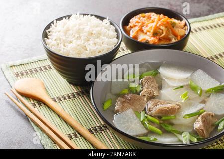 Koreanische Rindfleisch-Rettich-Suppe, soegogi muguk genannt, serviert mit Reis und Kimchi Nahaufnahme auf der Matte auf dem Tisch. Horizontal Stockfoto