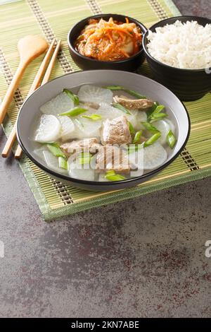 Muguk ist eine einfache Suppe mit koreanischem Rettich und Rindfleisch, serviert mit Reis und Kimchi als Nahaufnahme auf der Matte auf dem Tisch. Vertikal Stockfoto