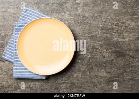 Draufsicht auf farbigem Hintergrund leere runde gelbe Platte auf Tischdecke für Lebensmittel. Leeres Gericht auf Serviette mit Platz für Ihr Design. Stockfoto