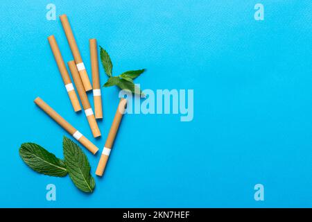 Menthol-Zigaretten und frische Minzblätter auf farbigem Hintergrund, viele Zigaretten gestapelt Draufsicht flach liegend. Stockfoto