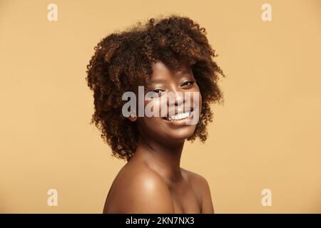 Porträt einer afroamerikanischen Frau mit sauberer, gesunder Haut auf beigefarbenem isoliertem Hintergrund. Lächelndes, wunderschönes, schwarzes weibliches Model. Stockfoto