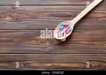 Vitaminkapseln in einem Löffel auf farbigem Hintergrund. Pillen als gesunde Mahlzeit serviert. Rote weiche Gel Vitamin-Supplement-Kapseln auf Löffel. Stockfoto
