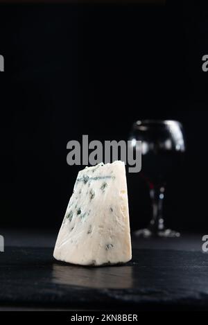 Eine Scheibe Roquefort-Käse mit blauem Schimmelpilz auf dunklem Hintergrund. Nahaufnahme mit Kopierbereich. Stockfoto