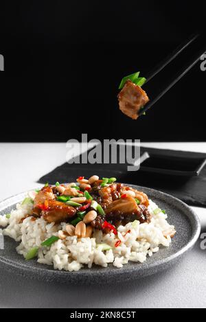 Asiatische Küche. Die Hand einer Frau hält asiatische Essensstäbchen. Reis mit Huhn auf grauem Hintergrund von oben. Gekochter Reis mit gebratenen Scheiben Stockfoto