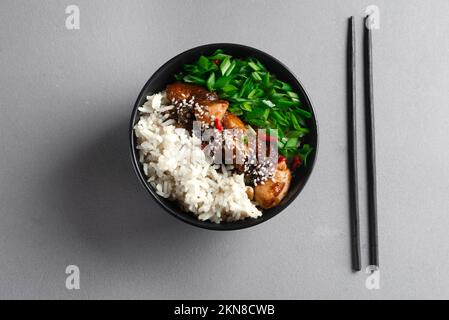 Reis mit würzigem Kung pao-Huhn auf einem Teller. Draufsicht. Schwarzer Teller mit asiatischem Essen Stockfoto